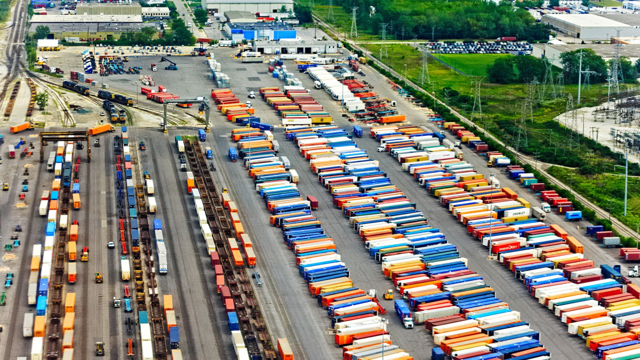 an bird's eye view of a shipping yard with hundreds of multi colored shipping containers and rail yard for intermodal transportation