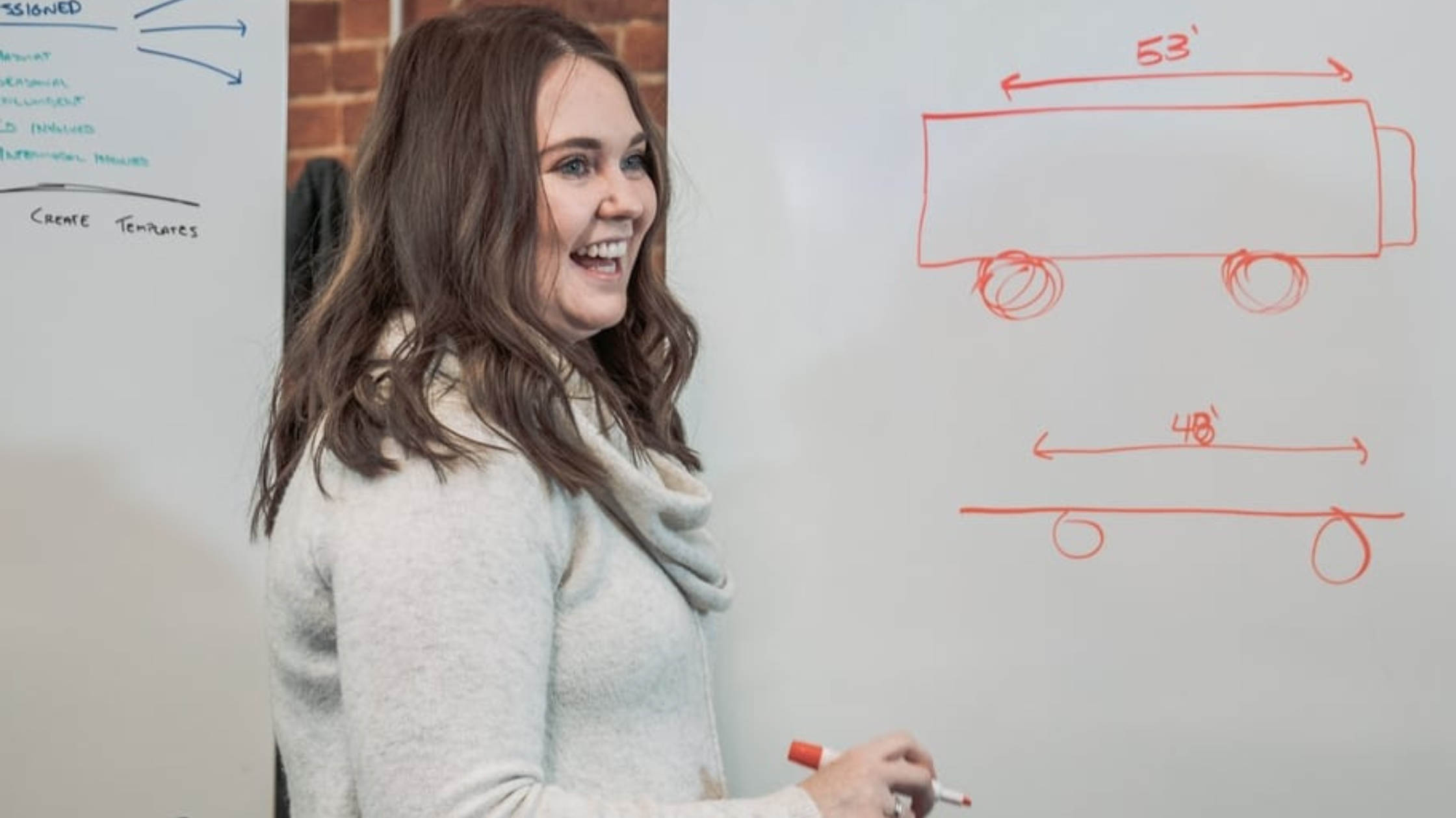 a women in trucking is in a white sweater standing at a white board drawing